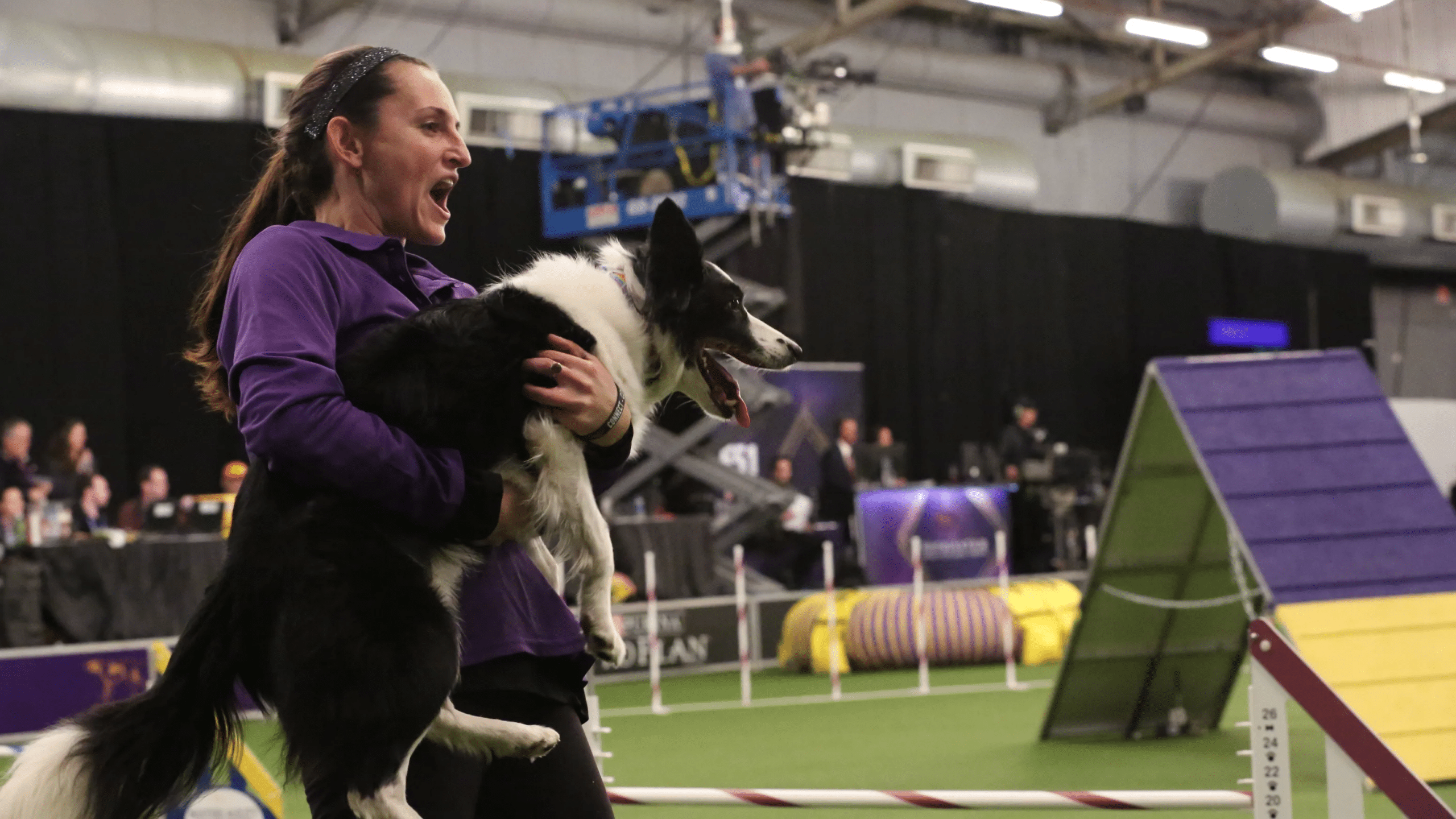 A woman holding a black and white dog at an event.