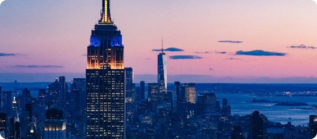 The empire state building is lit up at dusk in new york city.