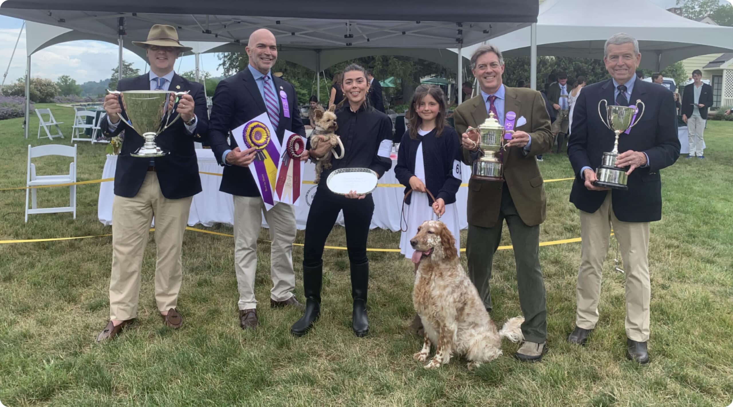 A group of people holding trophies in front of a tent.