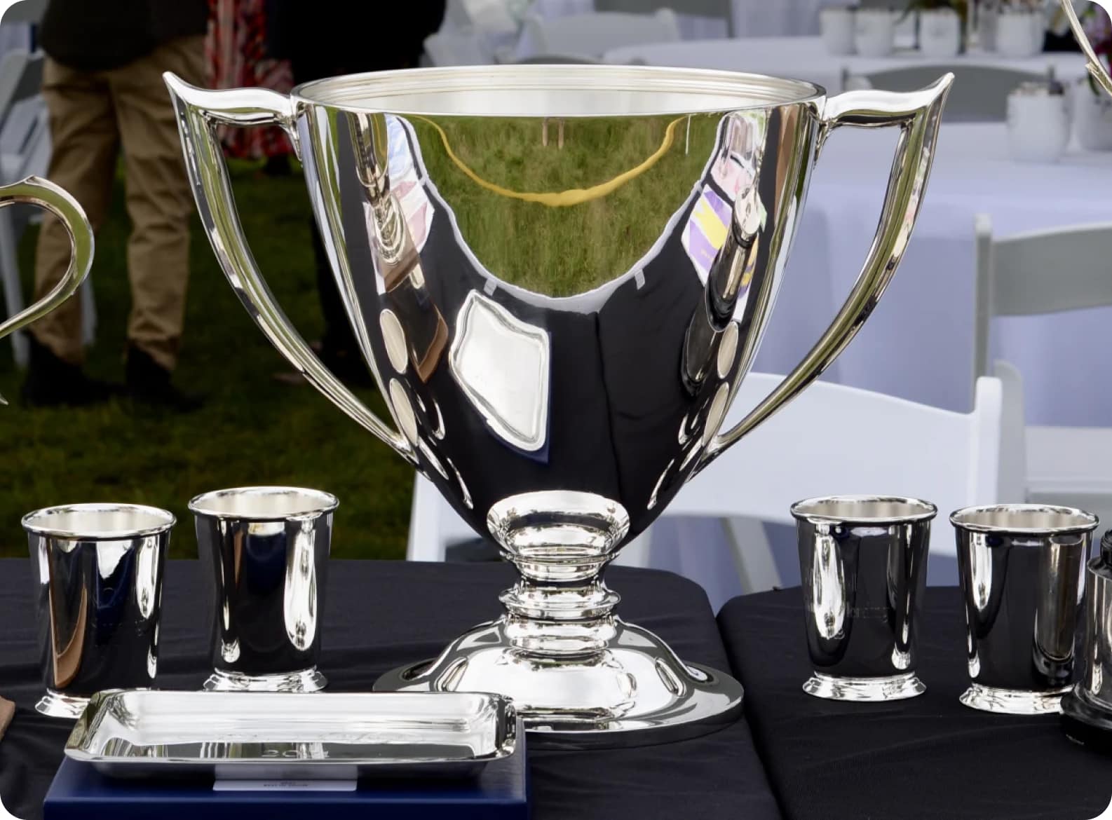 A silver trophy and silver cups on a table.