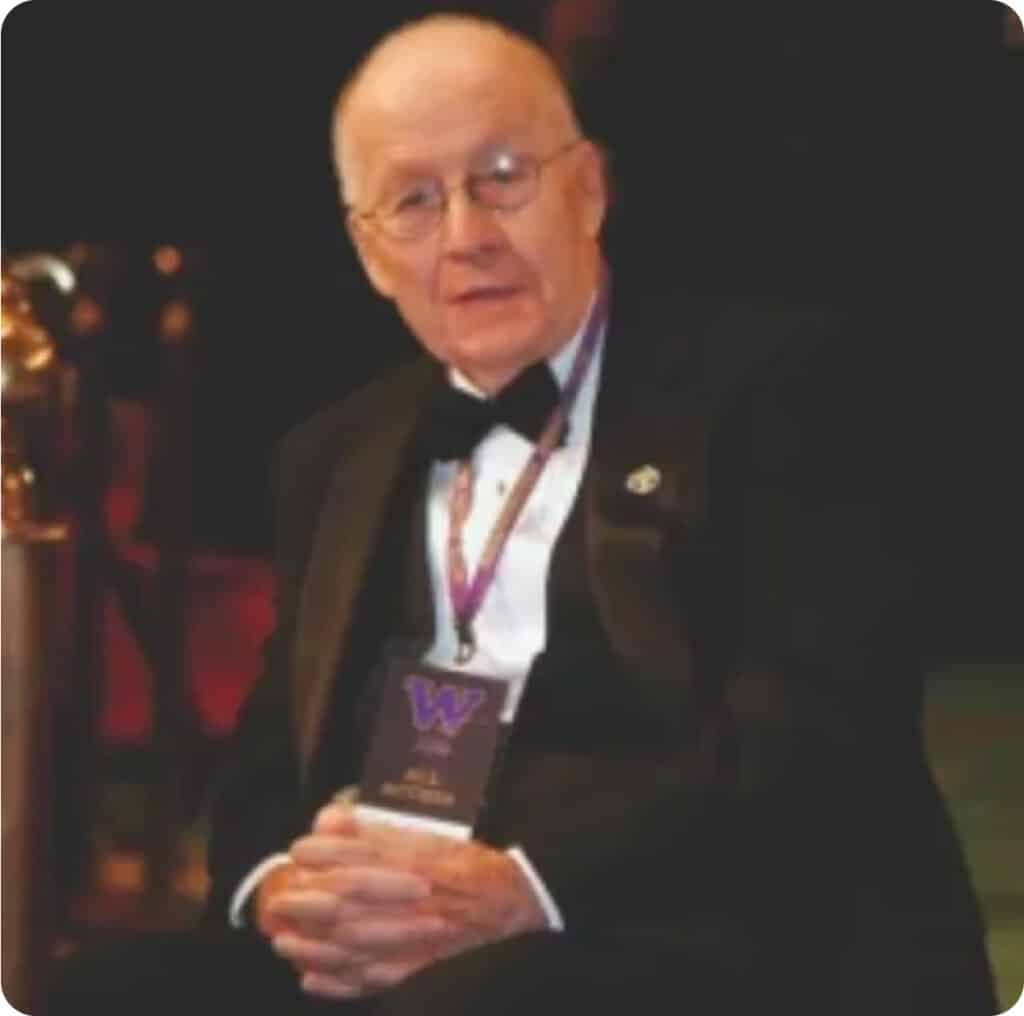 An older man in a tuxedo sitting on a chair.