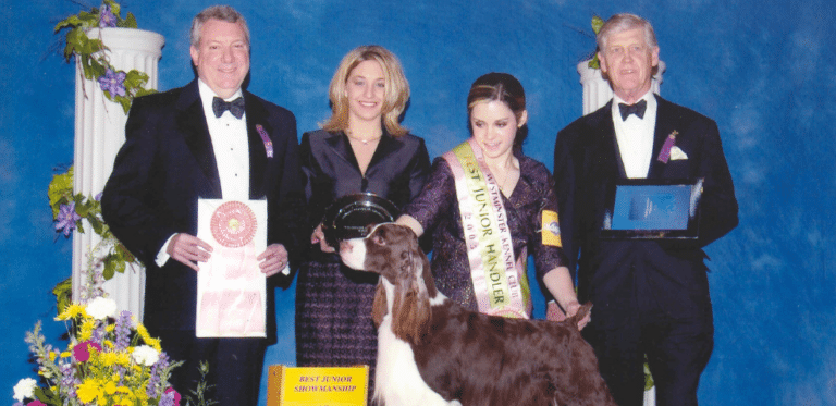 Four people in formal attire with awards stand beside a goat at an event.