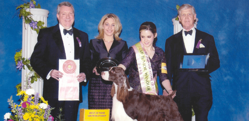 Four people in formal attire with awards stand beside a goat at an event.