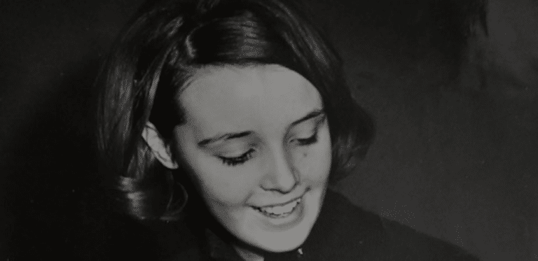 A black-and-white photo of a smiling young woman looking downwards.