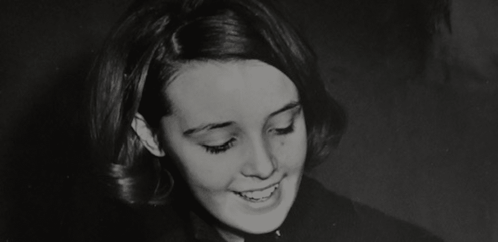 A black-and-white photo of a smiling young woman looking downwards.