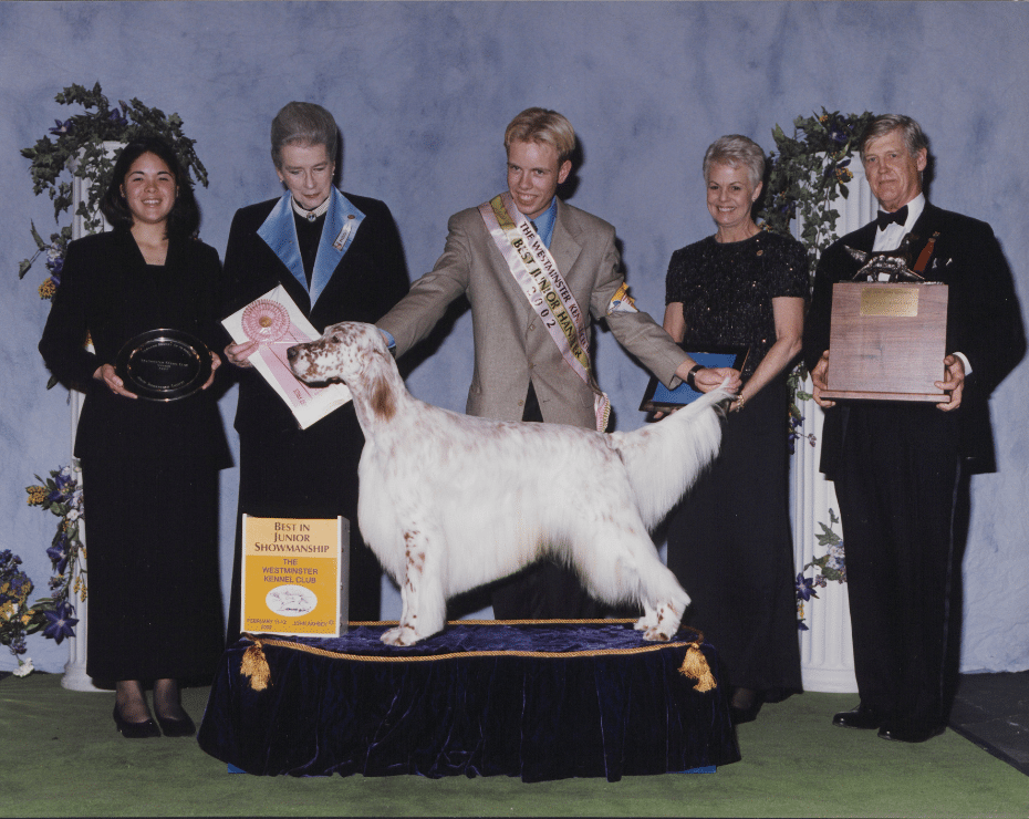Dog show winner on a podium with handlers and awards.