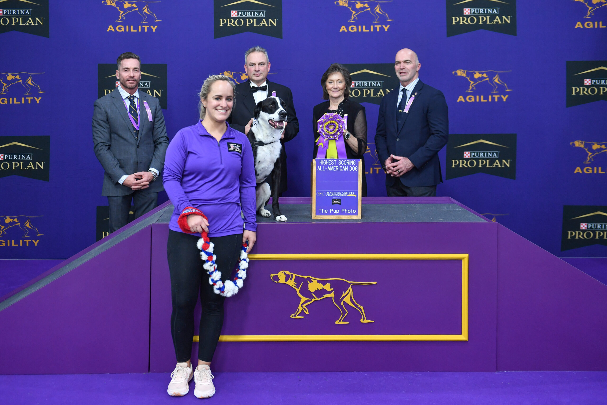 Meet Dr. Sara Lyle: The Westminster Kennel Club’s 2025 Veterinarian of the Year, as she and her dog stand on a winner’s podium with a ribbon, surrounded by four officials at a Purina Pro Plan agility competition event.