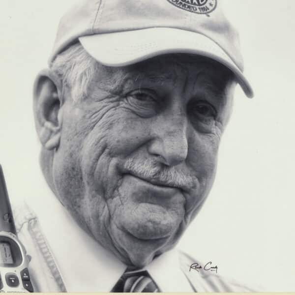 An older man wearing a cap and collared shirt looks at the camera, holding a walkie-talkie. The image is in black and white.