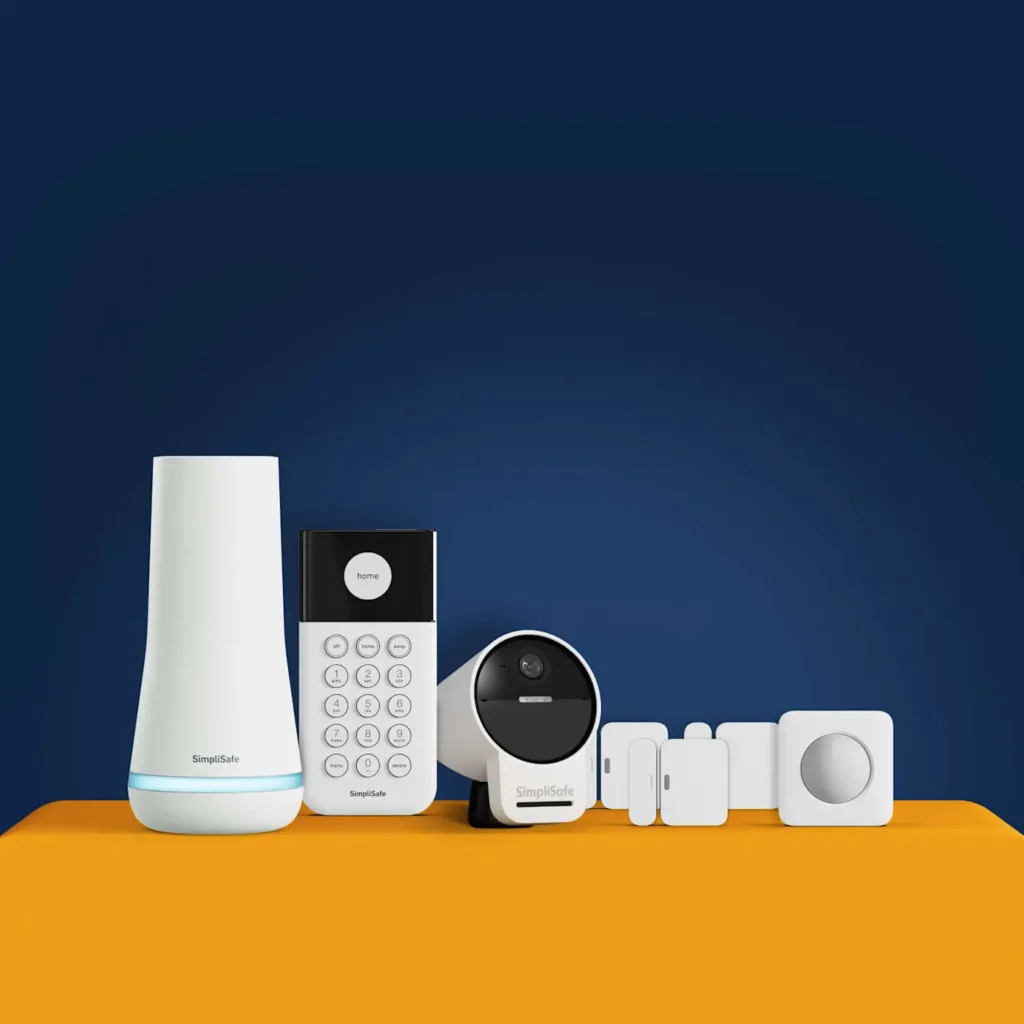 A SimpliSafe home security system set, including a base station, keypad, camera, sensors, and a panic button, arranged on an orange surface against a dark blue background.