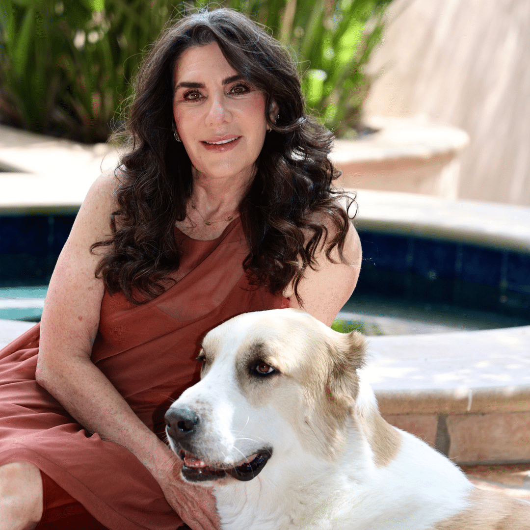 A woman with long dark hair in a sleeveless brown dress sits by a pool, resting her arm on a large white and tan dog—the loyal companion of this Veterinarian of the Year.